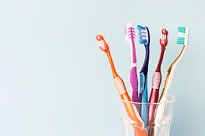 Multiple toothbrushes of different colors in a cup next to the sink.